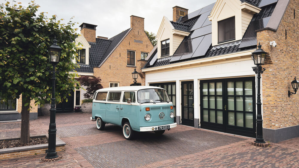 De VW-bus in de straat, met boom en herenhuis op de achtergrond.