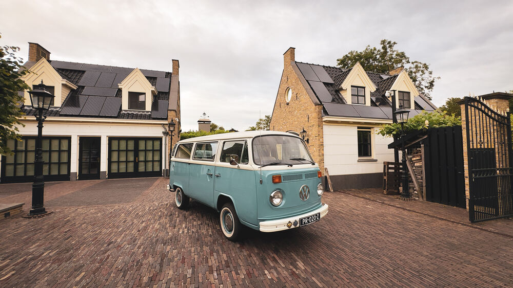De VW-bus schuin van achteren bij de garage, chroom glanzend.