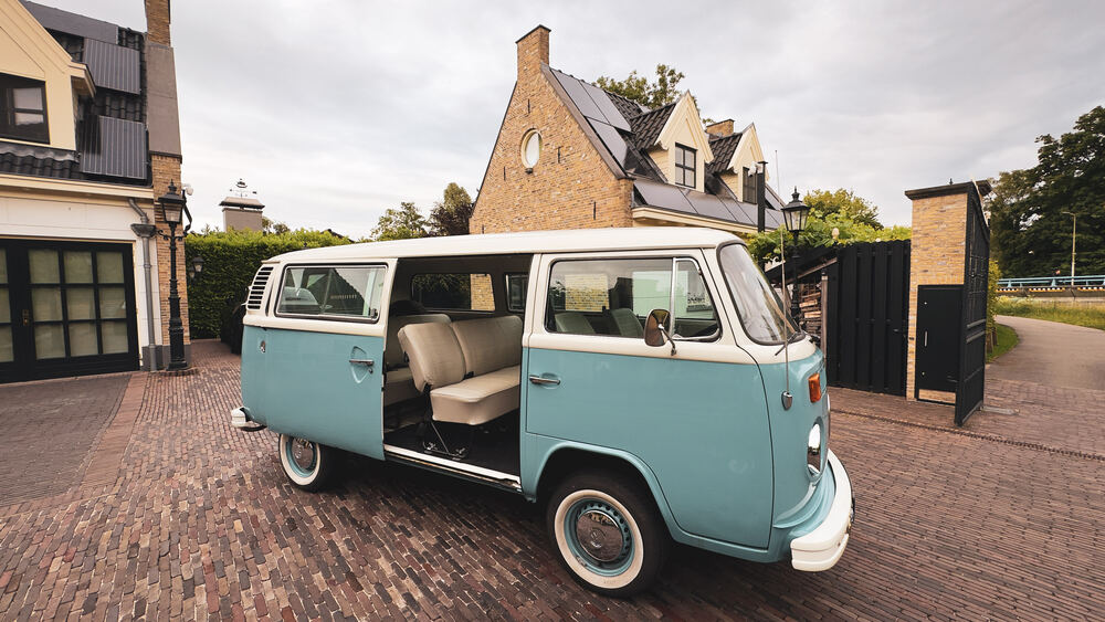 De VW-bus van opzij met geopende schuifdeur en zicht op de crème bank.