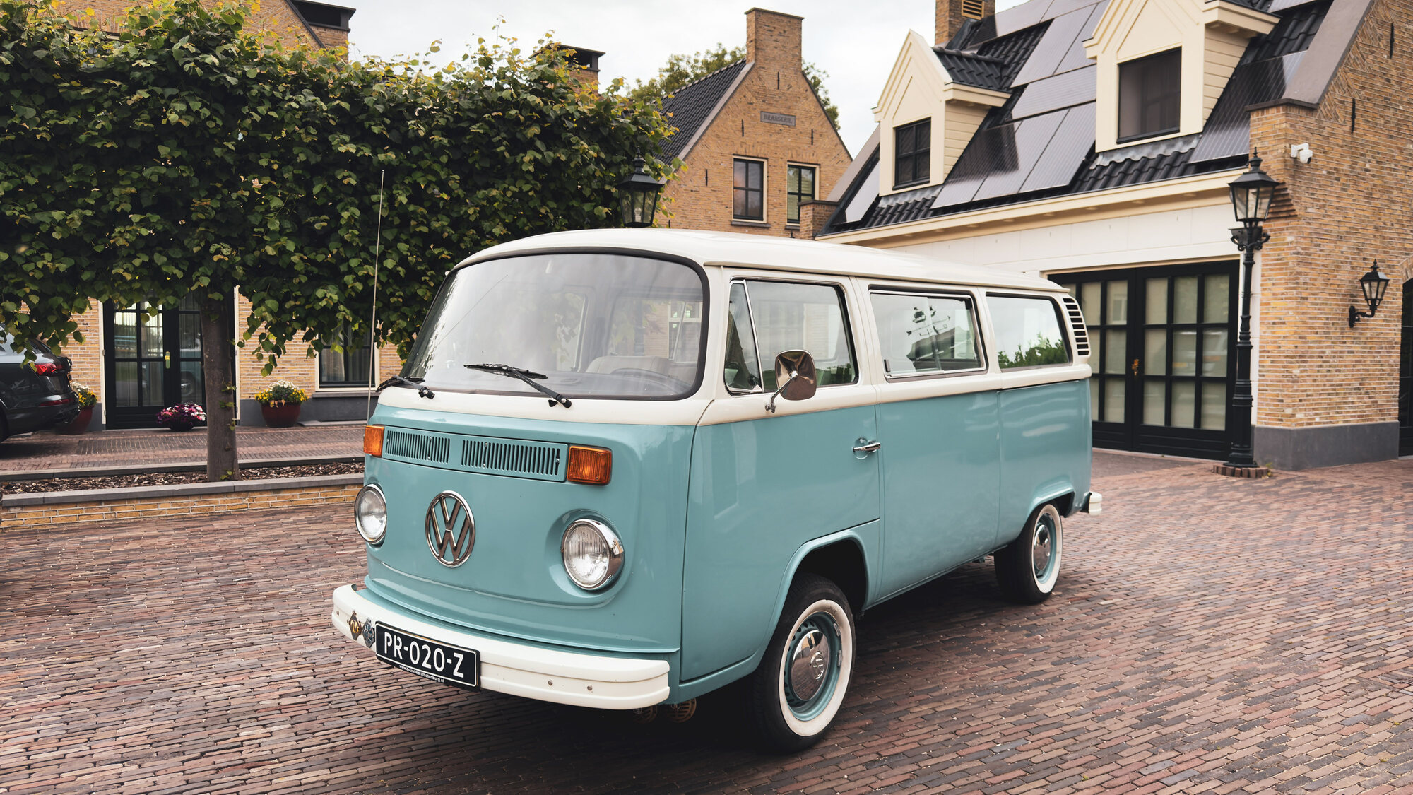 Zeegroen-met-crème Volkswagen T2 uit 1978 op de klinkers voor een Nederlands herenhuis op een rustige zondagochtend.